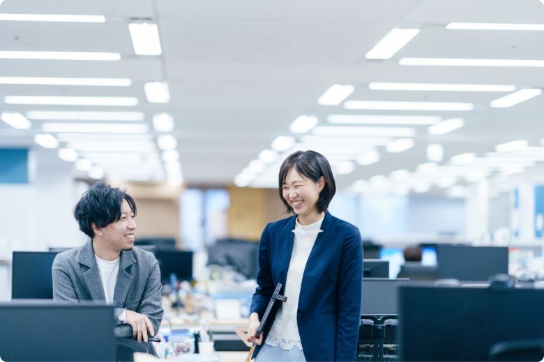 広く開放的なオフィスで笑顔の社員2人組。