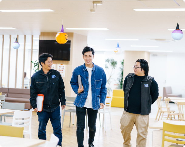 オフィスの共用スペースで、楽しそうに話しながら歩く3人の社員。
