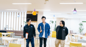 オフィスの共用スペースで、楽しそうに話しながら歩く3人の社員。
