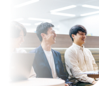 会議室で打ち合わせをしているビジネスパーソンたち。テーブルを囲んで5人の男女が和やかに会話をしながら、ラップトップや資料を活用して意見を交わしている。